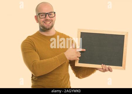 Portrait de jeune homme musclé chauve happy smiling while holding and pointing at blank blackboard Banque D'Images