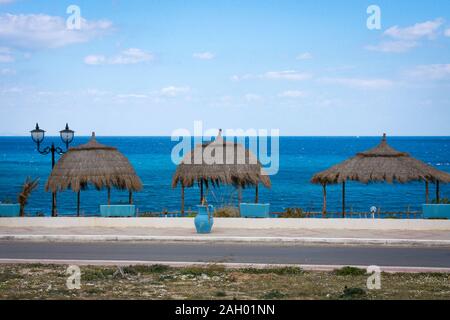 Un pot bleu sur la promenade du bord de mer surplombant la mer Méditerranée avec quelques ombrages en chaume à Hergla, Tunisie Banque D'Images