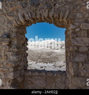 Vue d'une ouverture des murs de Rocca Calascio sur les montagnes enneigées du Gran Sasso d'Abruzzo, chaîne de montagne en Italie Banque D'Images