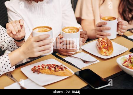 Les amis ou collègues à boire du café et manger des hot-dogs pour le déjeuner dans le café Banque D'Images