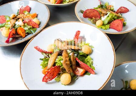 Filet de poisson frit avec salade de rougets. Tendre le filet d'agneau poêlé au semoule de maïs, des herbes fraîches, des tomates cerises, des craquelins de pommes de terre et la sauce au thon. Banque D'Images