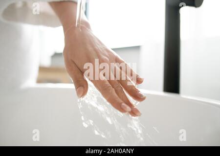 Main de jeune femme sous l'eau chaude pure découlant de puiser dans une baignoire Banque D'Images