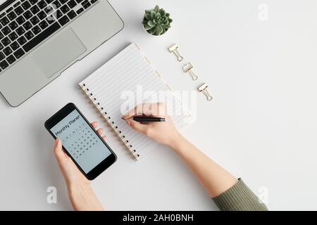 Mains de femme employée holding smartphone et un stylo sur la page blanche d'un ordinateur portable. Banque D'Images