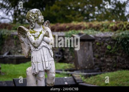 KILKENNY, IRLANDE, LE 23 DÉCEMBRE 2018 : Sculpture d'un vieil Ange chérubin creepy au milieu d'un cimetière, plein de lichen et moule, tenant sa poitrine Banque D'Images