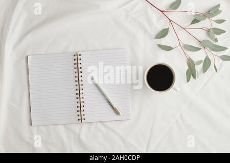 Flatlay d'open notebook avec des pages blanches et un stylo, tasse de café noir et des plantes Banque D'Images