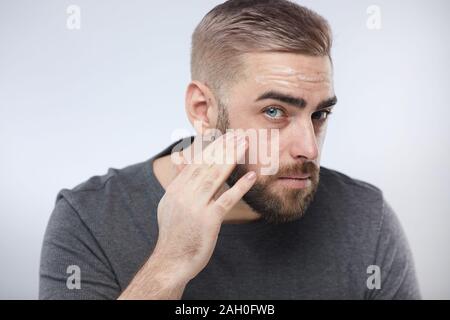 Close up portrait of horizontal tourné de beau barbu hydratant visage massage crème dans sa peau, fond blanc Banque D'Images