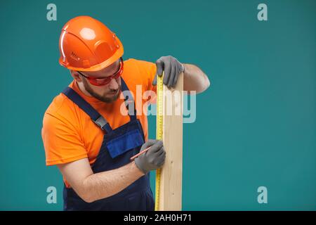 Portrait studio horizontal de carpenter wearing orange et bleu taille uniforme planche en bois, fond bleu turquoise Banque D'Images