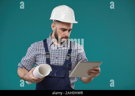Studio moyen portrait of Caucasian permanent ingénieur contre mur turquoise bleu plan holding building and using tablet computer Banque D'Images