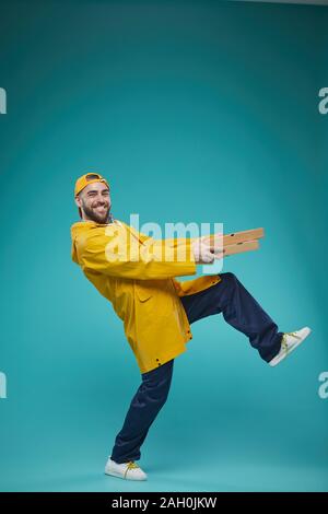 Studio full shot portrait d'jooyful travailleur à temps partiel portant uniforme jaune livraison pizza, copy space Banque D'Images