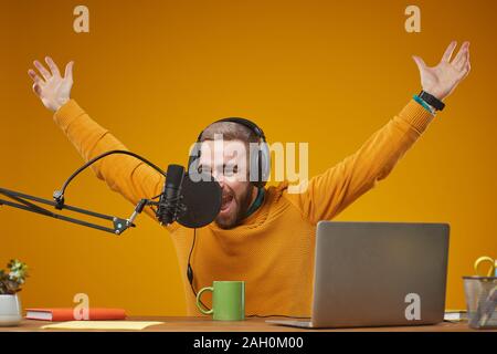 Moyenne horizontale studio portrait of joyful young Caucasian man wearing headphones enregistrement de contenu pour ses abonnés Banque D'Images