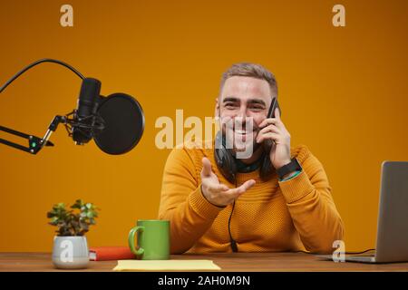 Studio horizontale portrait de jeune homme assis à l'animateur de radio 24 avoir appel téléphonique pendant les pauses, le backround de moutarde Banque D'Images