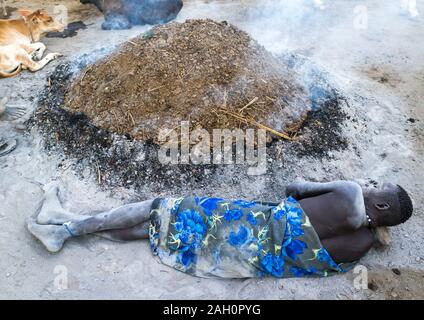 Mundari homme tribu reposant sur un oreiller en bois en face d'un feu fait avec dungs vache séchées pour éloigner les moustiques, l'Équatoria central, Terekeka, AFRIQUE DU S Banque D'Images