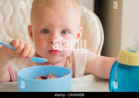 Garçon d'apprendre à manger. cute baby malpropre manger des légumes avec cuillère par vous-même dans une chaise haute. Banque D'Images