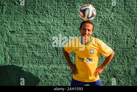 Un fan de football brésilien dans son équipe nationale's couleurs montrant outre de son sourire amical ainsi que ses compétences avec un ballon de football. Banque D'Images