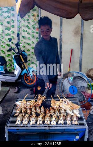 Un jeune homme Faire cuire la viande sur un barbecue, Phnom Penh, Cambodge. Banque D'Images