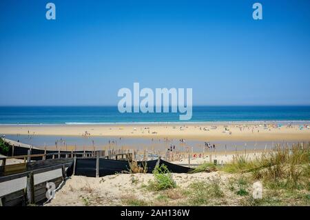 Acier bleu ciel au-dessus d'une plage bondée à bleu océan atlantique en france avec sol en bois clôture en premier plan Banque D'Images