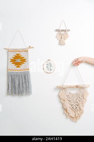 Woman hand holding macrame tapestriy à côté de ceux déjà accroché au mur Banque D'Images