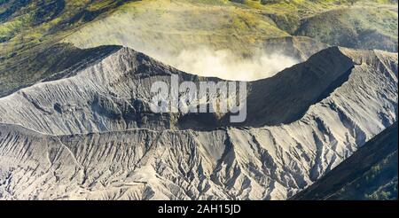 Vue rapprochée du Mont Bromo cratère dans l'avant-plan et de vertes collines au loin pendant un beau coucher du soleil. Banque D'Images