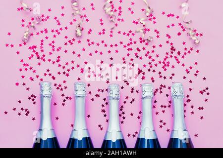 Cinq bouteilles de Champagne de confettis étoile et banderoles parti sur fond rose. Copier l'espace, vue d'en haut. Mise à plat de Noël, anniversaire, bachelorett Banque D'Images