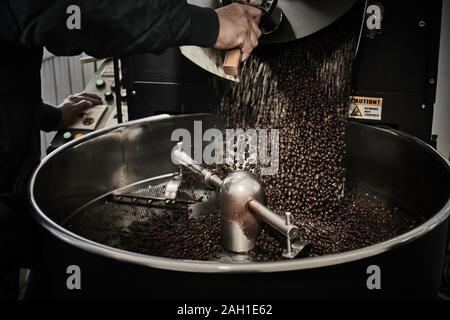 Verser les grains de café fraîchement torréfié provenant d'un grand torréfacteur de café dans le cylindre de refroidissement. Banque D'Images