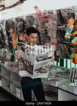 Engrossed Young Man Reading News at Magazine and Newspaper Shop, Latest Headlines, Street News, public, Urban Lifestyle, informations, événements en cours Banque D'Images