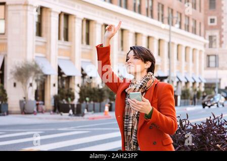 Jolie jeune femme demande un trajet à partir d'un super pilote sur une rue de ville en maintenant un téléphone cellulaire Banque D'Images