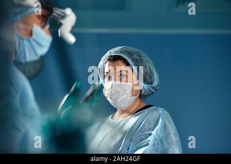 Deux chirurgiens en uniforme de protection au cours de l'opération, sur fond de salle de chirurgie. Banque D'Images