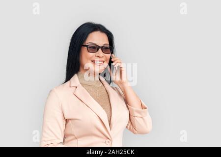 Freestyle. Asian businesswoman in eyeglasses isolés sur fond blanc en conversation sur joyeuse smartphone Banque D'Images