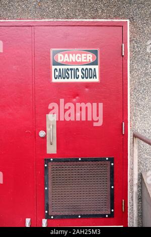 La soude caustique panneau d'avertissement sur une porte rouge, près d'une usine de traitement de l'eau dans la région de Renton, Washington, USA ; danger de la soude caustique. Banque D'Images