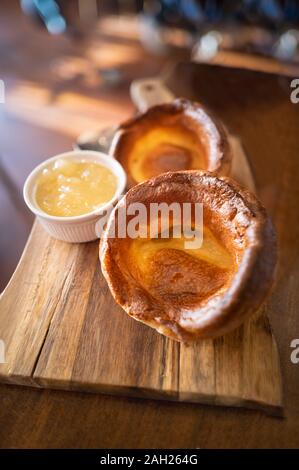 Deux gros Yorkshire puddings savoureux sur un plat de service en bois avec de la compote de pomme dans un plat servi en accompagnement de rôti de porc pour un traditionnel Fra Banque D'Images