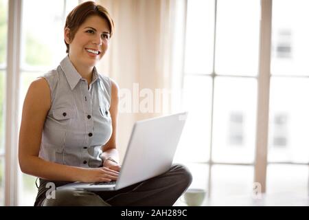 Mid adult woman sitting on a table lors de l'utilisation d'un ordinateur portable. Banque D'Images