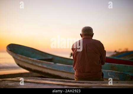 Pensive man assis sur une plage au coucher du soleil. Banque D'Images