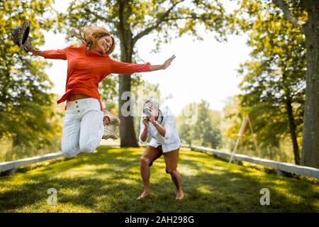 Man photographing son épouse sautant en l'air dans un parc Banque D'Images