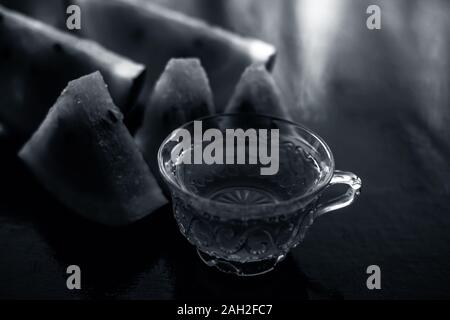 Melon d'eau à la bouche du thé dans une tasse en verre transparent sur la surface en bois avec des morceaux de pastèque en forme de triangle. Banque D'Images