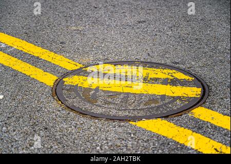 Les lignes jaunes double peint sur un couvercle de trou d'humour à effet. Banque D'Images