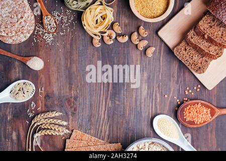 Différents types d'aliments riches en glucides. La farine, du pain, pâtes sèches et les lentilles et d'autres ingrédients sur la table en bois. Banque D'Images