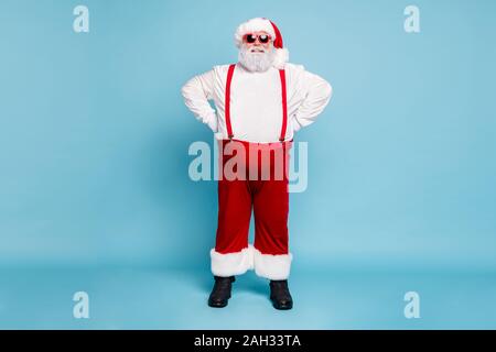 Longueur Fulle photo de funny funky aux cheveux gris et un excès de graisse santa claus hat avec lunettes moderne profiter de Noël du temps, l'usure beau rouge salopette Banque D'Images