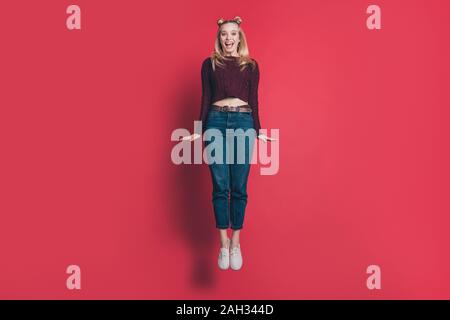 Photo pleine longueur de funny lady attrayant de sauter de joie en vol haut tricoté usure bourgogne pull et jeans pastel couleur rouge isolé Banque D'Images