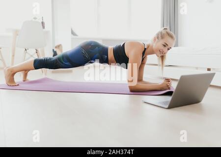 Femme sportive concentré durables est en train de faire l'élaboration à la maison et faisant partie de l'avant de son ordinateur portable, le port de vêtements de sport Banque D'Images