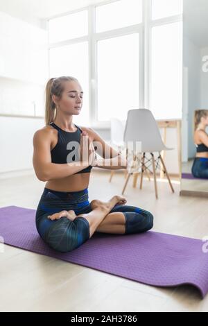 Young caucasian woman practicing yoga, appréciant matin home workout dans Lotus présentent pour l'heure de méditation, pleine longueur, isolé, plus white studio Banque D'Images