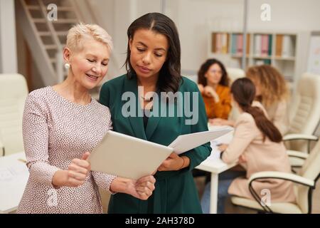 Femme mature montrant quelque chose sur son ordinateur tablette à son jeune collègue coup horizontal Banque D'Images