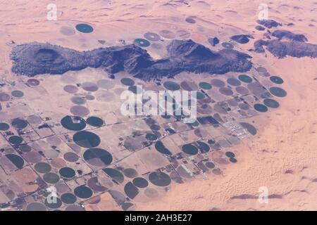 Vue aérienne de l'irrigation des champs et fermes ronde entourée de dunes de sable dans le désert en Arabie Saoudite Banque D'Images