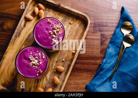 Vue de dessus de deux verres avec du violet berry smoothie sont servis aux amandes concassées sur un plateau en bois Banque D'Images