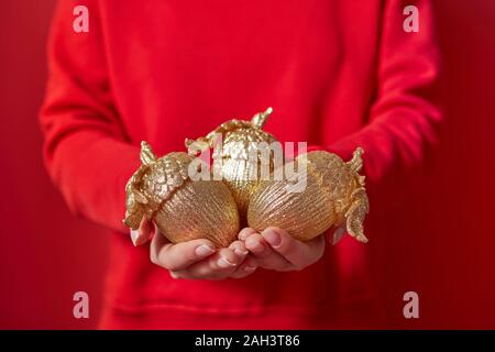 Décoration de Noël les glands dans le golden big woman's hands sur l'arrière-plan de vêtements rouge avec copie espace. Carte de vœux de Nouvel An. Banque D'Images