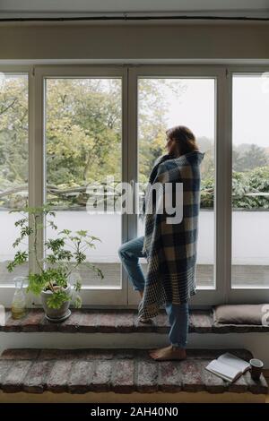 Femme à la fenêtre de sortie, enveloppé dans une couverture Banque D'Images