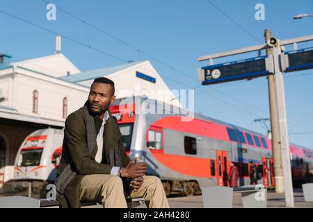 L'homme élégant avec tasse réutilisable attendant le train Banque D'Images