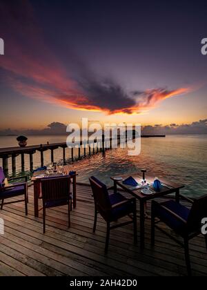 Les Maldives, table de salle à manger du restaurant côtières au crépuscule avec pier en arrière-plan Banque D'Images