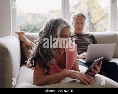 Senior couple relaxing on couch à domicile à l'aide de l'ordinateur portable et tablette Banque D'Images