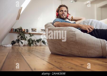 Young man relaxing in Pouf poire à la maison écouter de la musique Banque D'Images