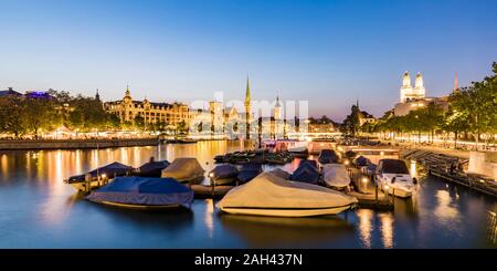 La Suisse, Canton de Zurich, Zurich, couverts bateaux amarrés sur la rivière Limmat au crépuscule à bord de la vieille ville en arrière-plan Banque D'Images